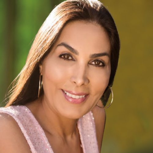 A woman with long dark hair, wearing a sleeveless pink top and hoop earrings, smiles at the camera against a blurred green and yellow background.